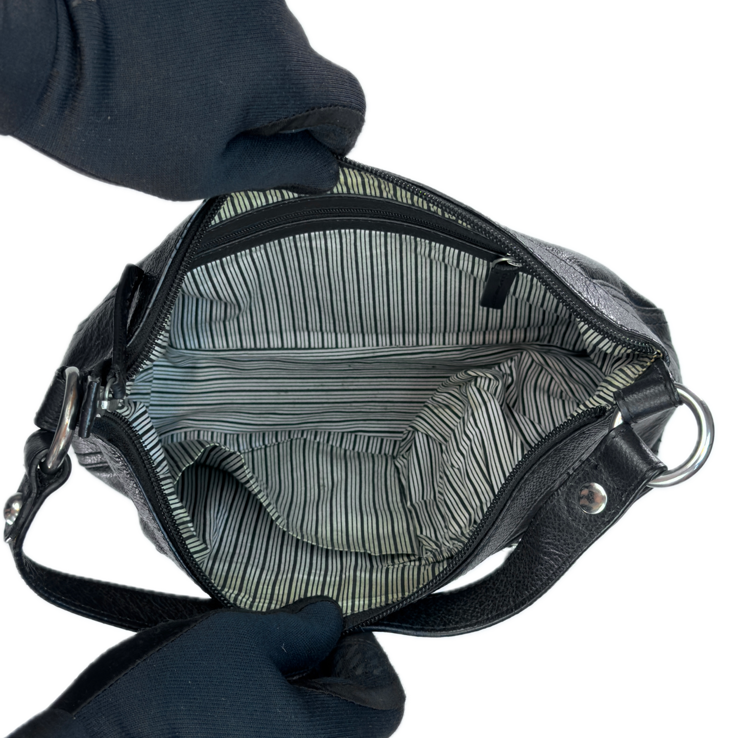 Top-down interior view of a vintage black leather baguette bag held open by black-gloved hands, revealing a clean retro black and white striped textile lining.