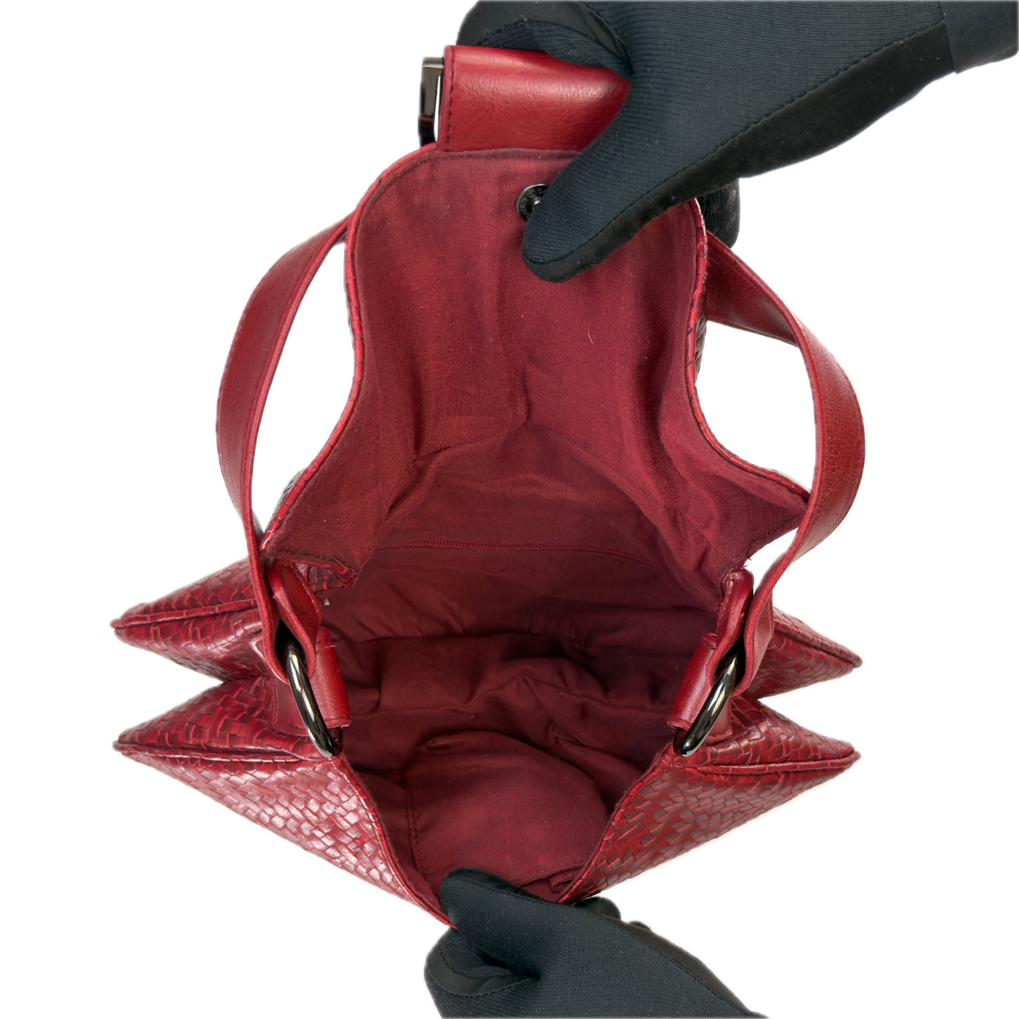 Top-down interior view of a vintage red woven baguette bag held open by black-gloved hands, revealing a clean red textile lining.