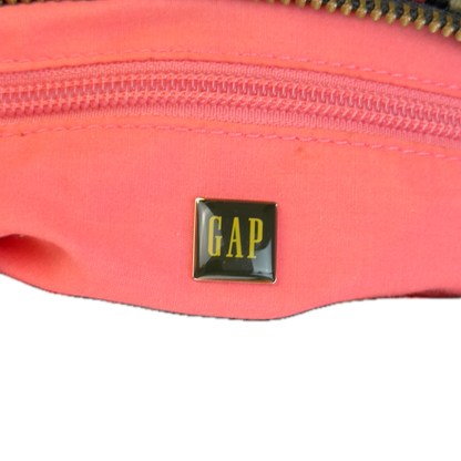 A close-up of a bag's bright pink interior with a gold-tone zipper, featuring a small square black and gold GAP logo patch on the front.