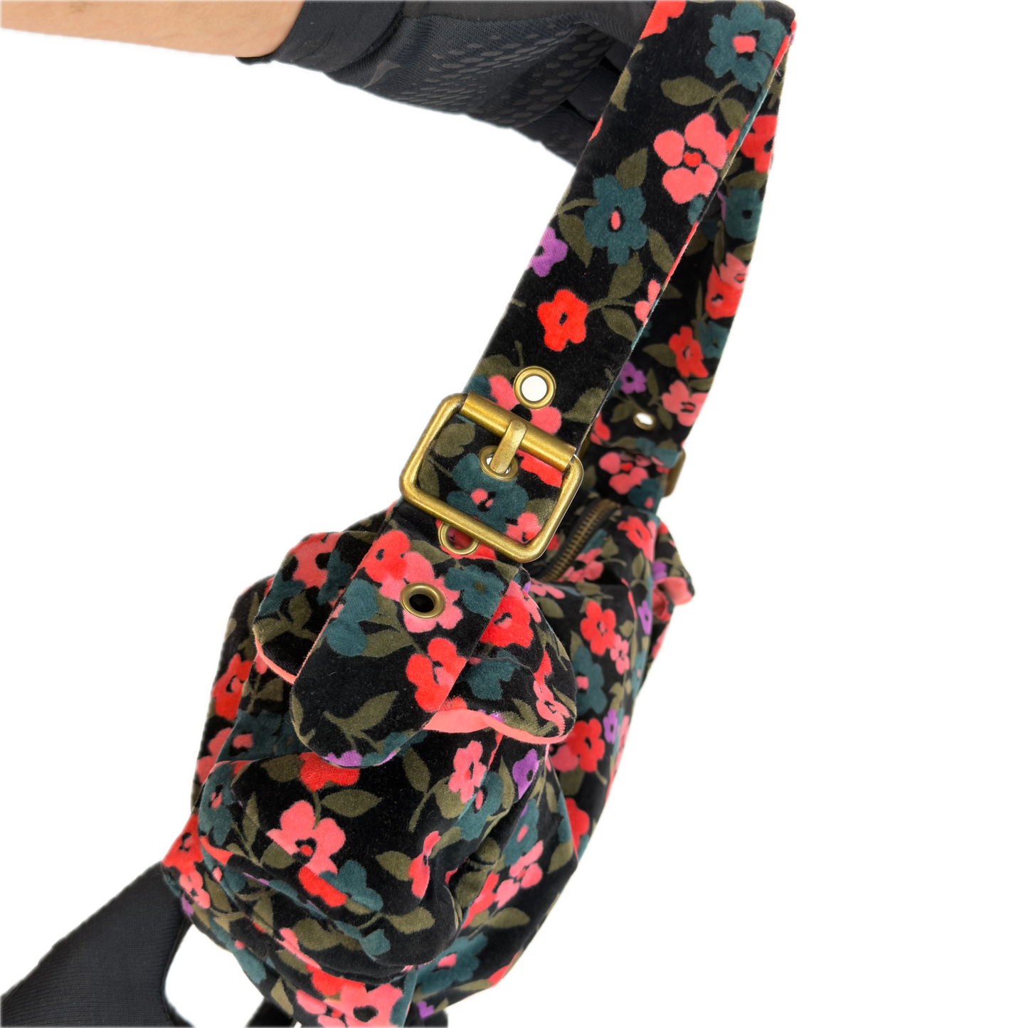 A close-up of a floral shoulder bag with a black velvet-like base and a dense print of pink, red, purple, and green flowers. The bag features a prominent gold-tone buckle and strap hardware, shown against a plain white background.
