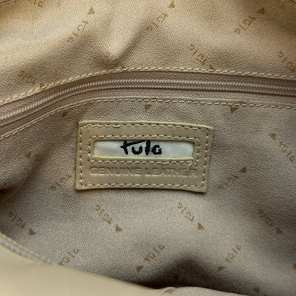 Close-up of the interior of a beige bag showing a stitched label that reads 'Tula' and 'Genuine Leather' on a patterned beige fabric.
