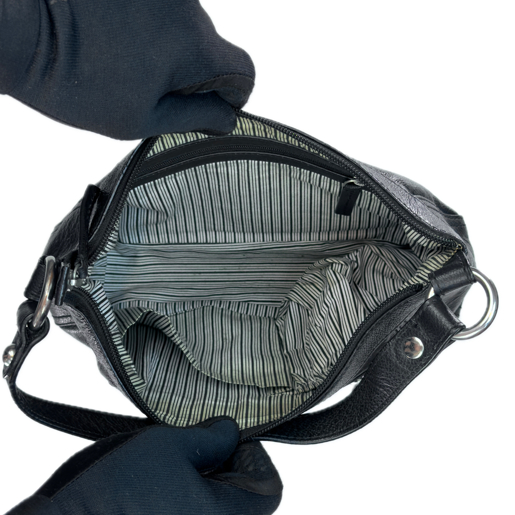 Top-down interior view of a vintage black leather baguette bag held open by black-gloved hands, revealing a clean retro black and white striped textile lining.