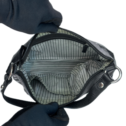 Top-down interior view of a vintage black leather baguette bag held open by black-gloved hands, revealing a clean retro black and white striped textile lining.