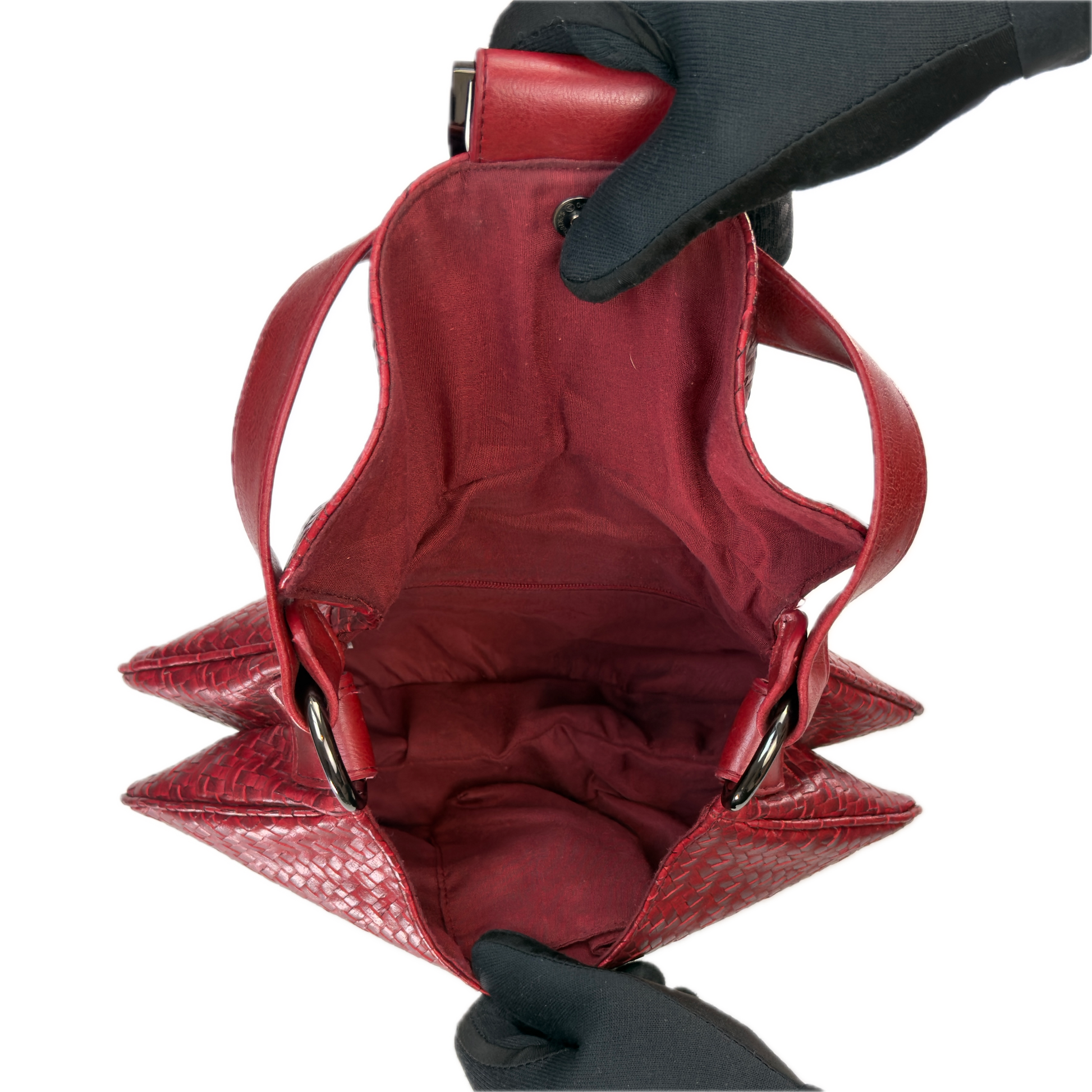Top-down interior view of a vintage red woven baguette bag held open by black-gloved hands, revealing a clean red textile lining.