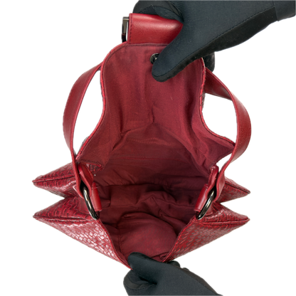 Top-down interior view of a vintage red woven baguette bag held open by black-gloved hands, revealing a clean red textile lining.
